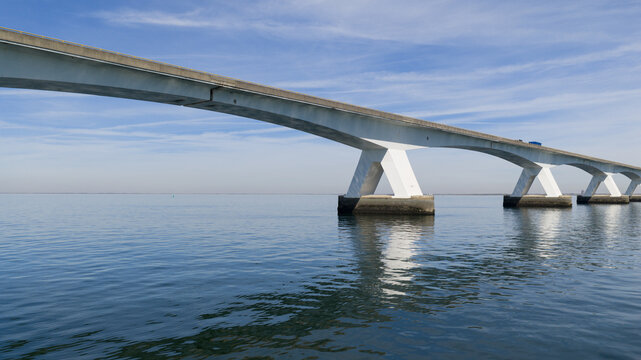 Aerial view of Zeeland Bridge with its distinctive V-shaped concrete pillars spanning across the calm blue waters of the Oosterschelde estuary at Zierikzee, Zeeland, Netherlands.