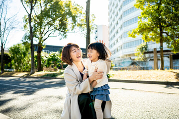 Naklejka premium Japanese mother hugging her toddler daughter in the park with soft sunlight