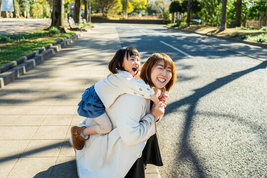 Joyful Japanese Mother and Little Daughter Laughing Together Outdoors in Sunlight