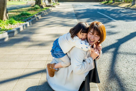 Happy Japanese Mother Carrying Little Daughter Piggyback in Sunny Park