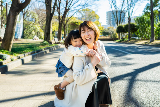 Joyful Japanese Mother and Little Daughter Laughing Together Outdoors in Sunlight