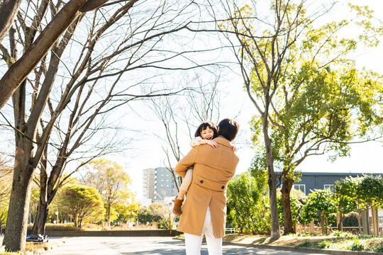 Rear View of a happy toddler girl being carried on her father's back in a public park, family bonding on a sunny winter day