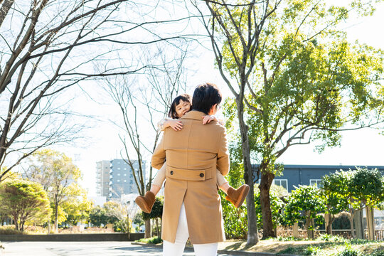 Rear View of a happy toddler girl being carried on her father's back in a public park, family bonding on a sunny winter day