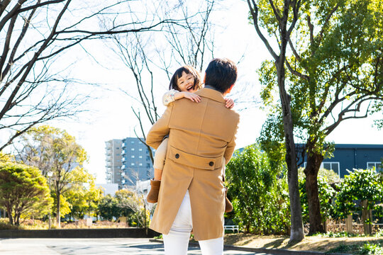 Rear View of a happy toddler girl being carried on her father's back in a public park, family bonding on a sunny winter day
