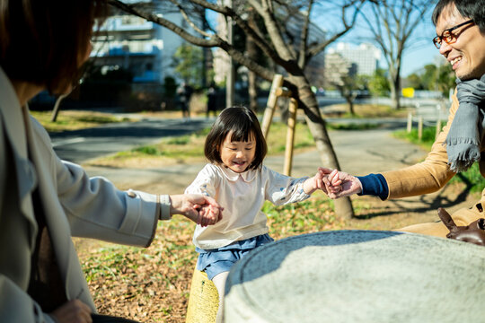 Little girl sitting on a park stool holding hands with both parents, family connection