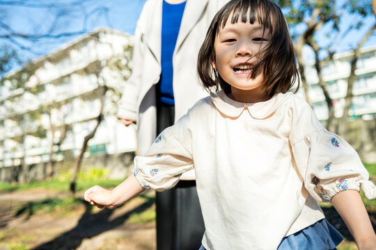 Portait of a cute Japanese toddler girl laughing with a big smile in a sunny park with parents in soft focus background