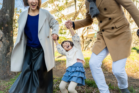 Joyful Japanese father lifting his laughing daughter high into the air at a sun-drenched winter park