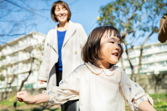 Portait of a cute Japanese toddler girl laughing with a big smile in a sunny park with parents in soft focus background