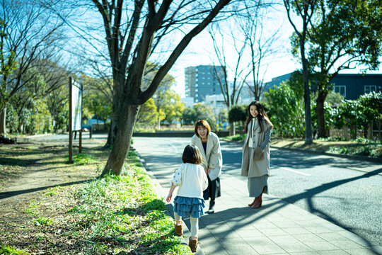Two Japanese women and a little girl talking and laughing in a sunny urban park
