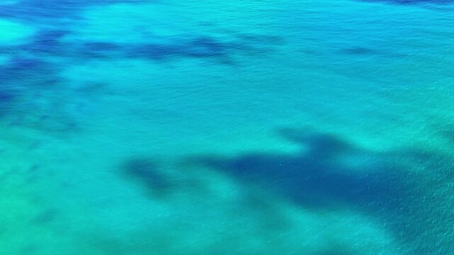 Blue background of sea water and coral shallows. Rippling water surface. Drone flight over the ocean. We fly above the sea. Seascape, rippling ocean waves. Turquoise wavy background.