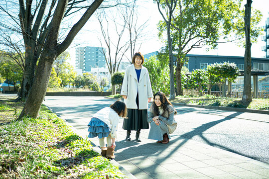 Japanese mother and friend crouching down to talk with a little girl in the park