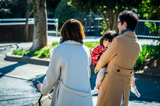 Back view of a Japanese father carrying his sleeping daughter while walking with mother