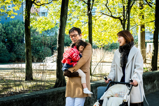 Happy Japanese parents walking together in a park while father carrying little daughter