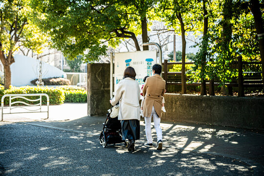 Back view of a Japanese family walking with a stroller in a bright sunny park