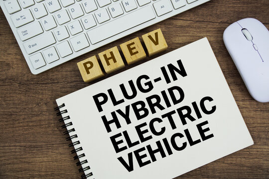 PHEV Plug-in Hybrid Electric Vehicle message with keyboard and optical mouse on wooden background