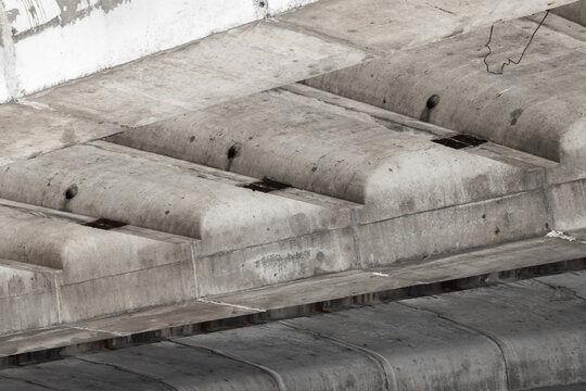 Underside of a weathered concrete bridge revealing reinforced beams, formwork impressions, stains and exposed fixings; a minimalist urban architecture study emphasizing industrial texture and geometry