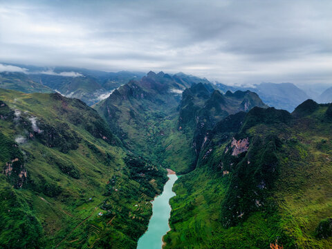 Aerial view of the turquoise Nho Que river winding through steep limestone mountains and lush green valleys of the Ha Giang Loop, Vietnam.