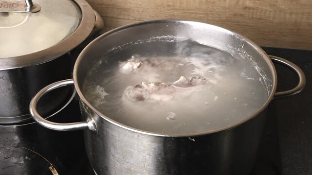 Close up of meat and bones gently boiling in clear liquid inside a stainless steel pot on a black induction stovetop in a home kitchen