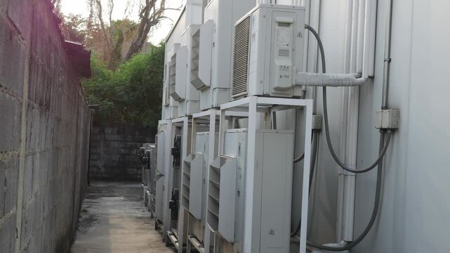 Row of outdoor air conditioner compressor units installed on wall in narrow alleyway with sunlight and lens flare