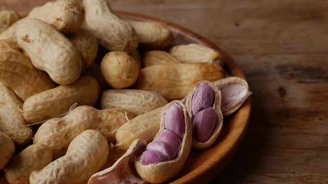 Boiled peanuts in shell with purple violet skin kernels revealed on wooden plate on rustic wood table, healthy traditional Asian snack nutrition closeup