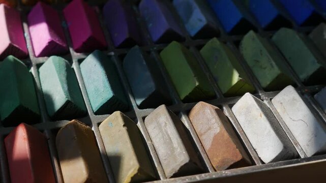 Colorful soft pastel chalk sticks arranged in a worn artist's palette box, vibrant rainbow art supply collection
