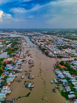Aerial view of the Hau River flowing through the city with floating houses, urban buildings, and a bridge under a blue sky in Chau Doc, An Giang, Vietnam.