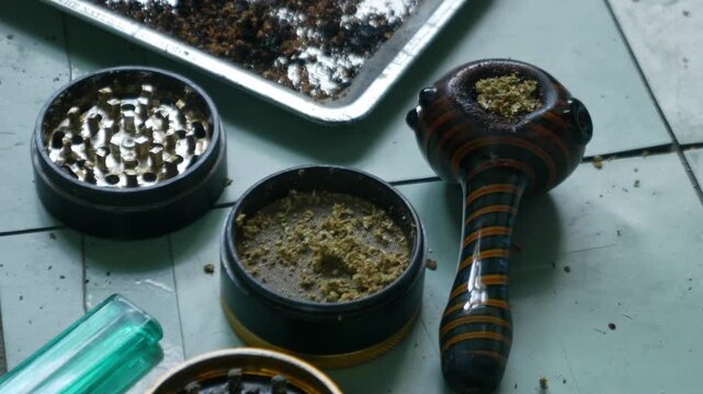 Glass Hand Pipe with Colorful Striped Design and Herb Grinder on Teal Table for Cannabis Lifestyle