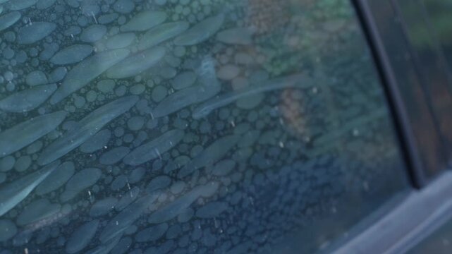 Air bubbles trapped in old deteriorated car window tint film, damaged adhesive layer on glass surface with peeling texture, vehicle maintenance problem and poor installation concept