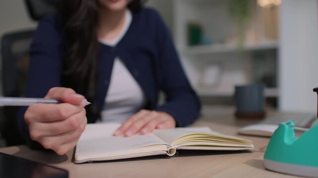 Modern Asian woman sitting in a cozy room, thoughtfully journaling in her notebook as part of her mindful morning routine, embracing slow living, self-reflection, intentional productivity