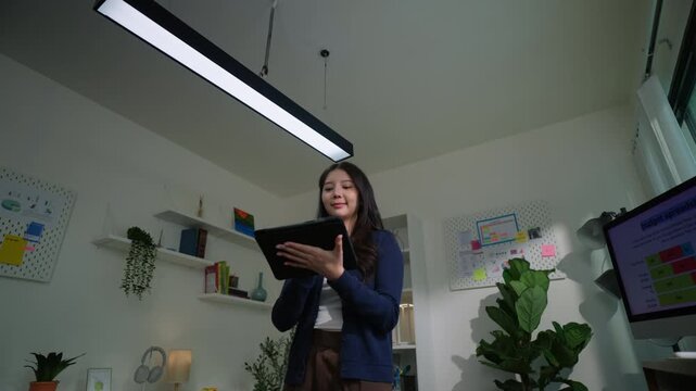 Modern woman adjusts smart lighting in her connected home office using a digital tablet, blending smart home tech, productivity, and comfort in a flexible, energy-efficient remote work environment