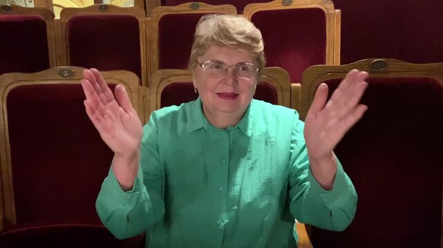 Senior happy woman is interested in watching ballet performance in theater hall, woman claps and enjoy