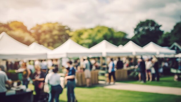 Outdoor market with white tents and people socializing on a sunny day, surrounded by trees and green grass.