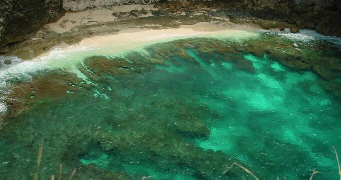 Overhead view of stunning turquoise ocean water waves washing onto narrow white sandy beach with rough rock formation