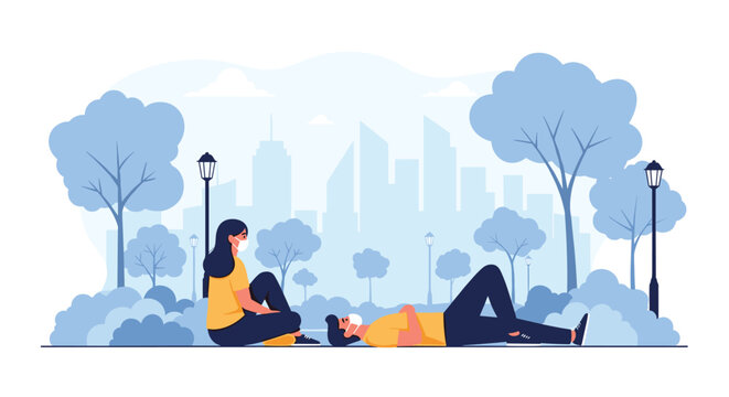 Couple wearing protective medical face masks relaxing in a city park with trees and skyline background while maintaining social distance.