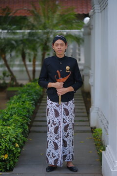 photo of a man in clothes from Yogyakarta, Indonesia holding a heirloom keris
