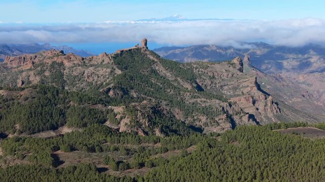 Stunning aerial perspective of the iconic Roque Nublo rock formation in Gran Canaria, with Mount Teide volcano visible above the clouds