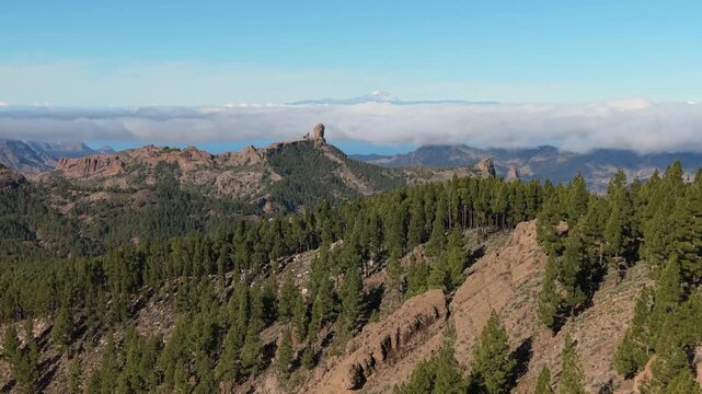 Majestic aerial view of the volcanic landscape of Gran Canaria, featuring Roque Nublo and Mount Teide above the clouds in the distance