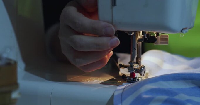 Focused hands guide blue fabric under the sewing machine's needle. The close-up captures the smooth stitching process and the skill required for perfect seams. 60 fps 4k footage.