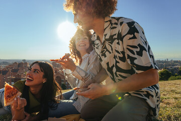 Young friends having outdoor pizza picnic with city view