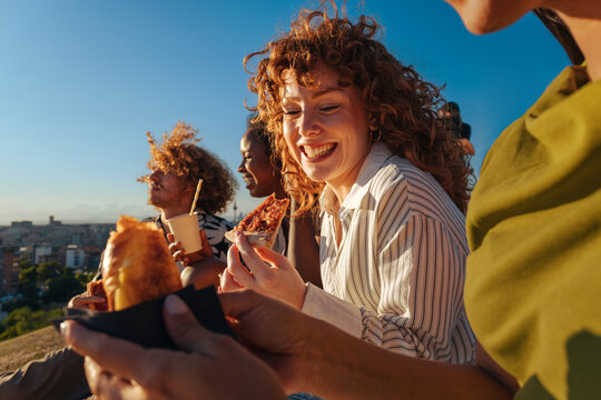 Diverse friends laughing eating pizza outdoors at sunset