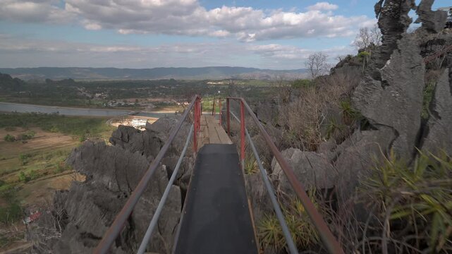 POV shot walking along a mountain ridge walkway with missing planks and boards, looking over a karst limestone landscape with a river below.