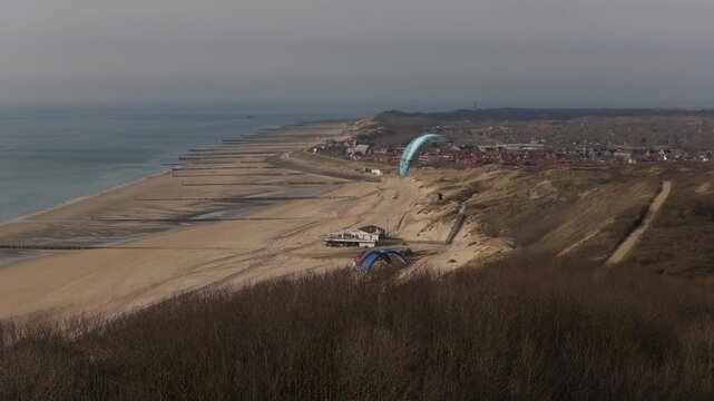 Drone passes behind vegetation revealing paragliders over Zoutelande coast