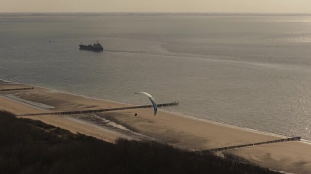 Drone follows paraglider over Zoutelande beach at sunset with boats on sea