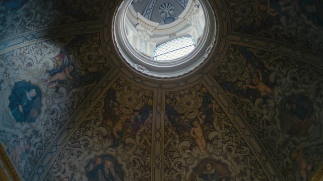 Ornate dome ceiling featuring detailed fresco paintings, angels, and religious figures illuminated by a central skylight in a historic interior.