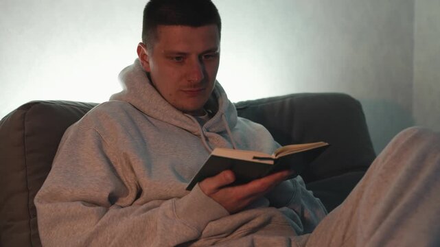 Young European man reading Bible in dark room. Concept of religion, faith, spirituality, Christianity, prayer, reflection, and spiritual study in calm indoor evening setting.