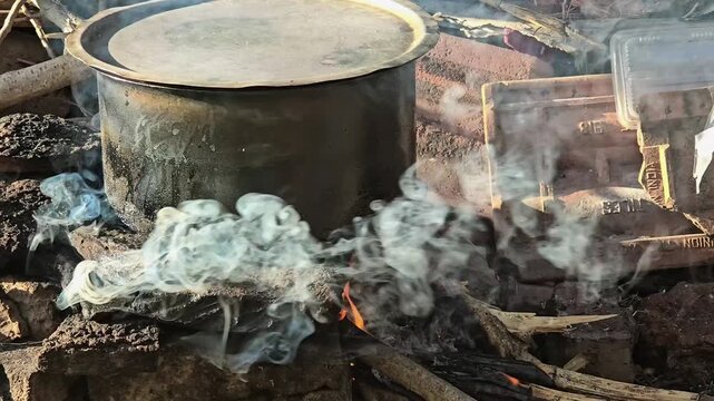 Facing resource shortages, a rustic metal pot simmers over an open wood fire. Thick smoke billows, marking a shift to natural fuel&mdash;a scene where traditional cooking becomes a need in a modern crisis.
