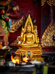 Obraz premium Ornate Gold Thai Buddha Statue with Floral Garland on Red and Blue Throne Surrounded by Ritual Offerings