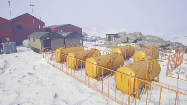 Aligned fuel containers across snowy field with fencing and pathways repetitive geometry of tanks creates rhythm distant red buildings and rocky outcrops frame