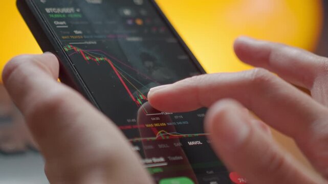 Person using smartphone with stock market charts on screen. Trader analyzing financial data on trading app. Concept of online trading, investment analysis and financial risk