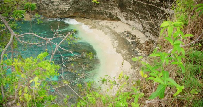 Scenic view small crescent white sand beach and turquoise water at bottom of steep cliff in Nusa Penida